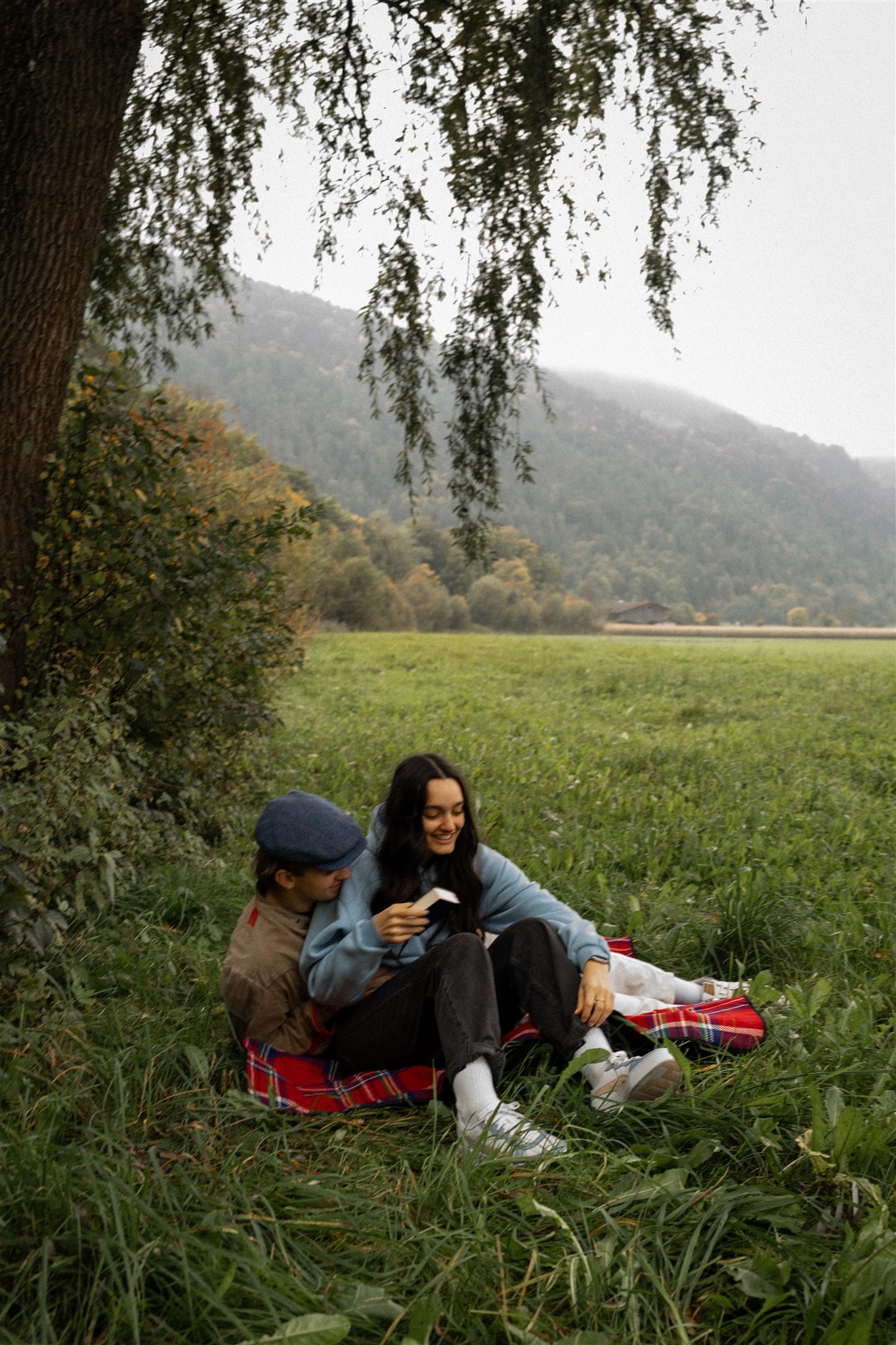 Cinematic photo of a couple sitting on a picnic blanket beneath a tree with a book
