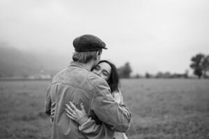 Black-and-white over-the-shoulder photo of a dreamy-looking woman embracing her partner