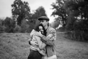 Black-and-white photo of a young couple embracing closely while gazing dreamily into nature