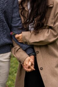 Close-up of a couple holding hands while the woman holds a flower