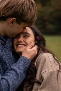 Close photo of a young woman looking lovingly at her partner while he kisses her forehead
