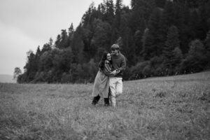 Black-and-white photo of a young couple laughing while walking across a meadow
