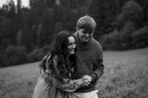 Close black-and-white photo of a young couple laughing while walking across a meadow with motion blur