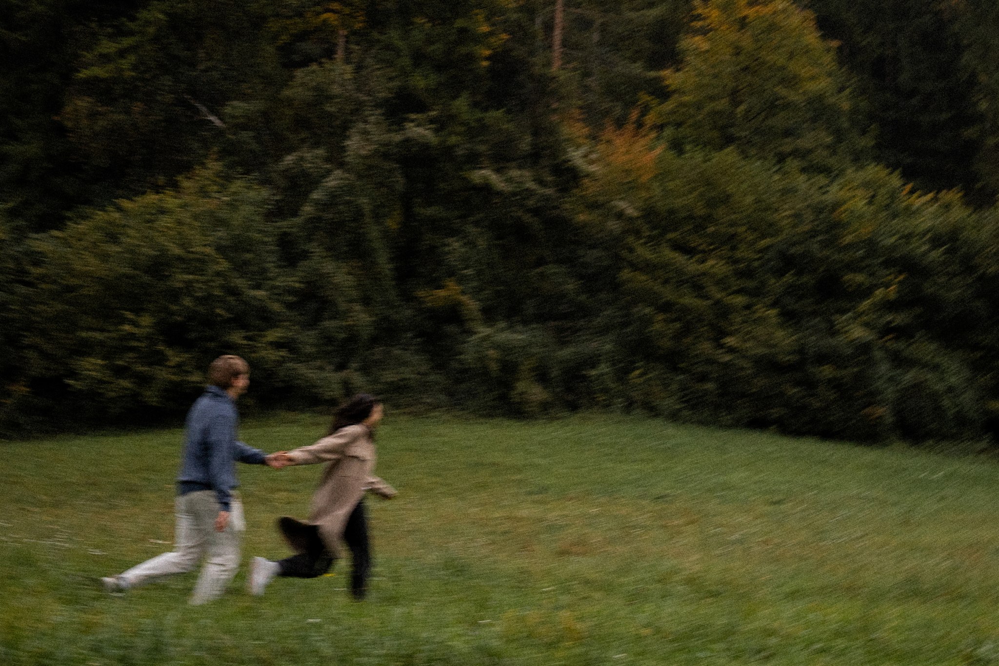 Vintage cinematic motion blur photo of a couple holding hands while walking across a meadow