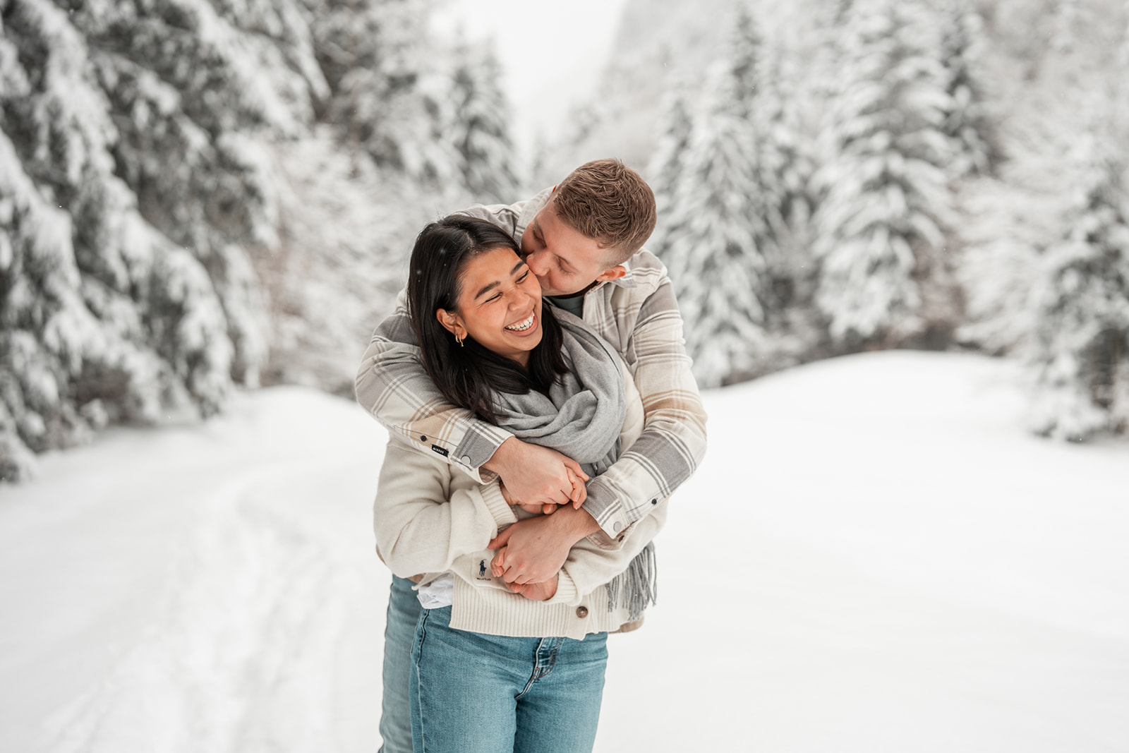 Medium close-up photo of a young couple with the man kissing his girlfriend on the cheek while she laughs