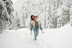 Young couple walking piggyback through a snowy field while laughing over their shoulders