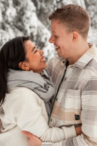 Young couple standing arm in arm in a winter landscape while smiling lovingly at each other