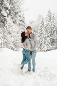 Couple standing wrapped in a scarf on a snowy field while laughing together