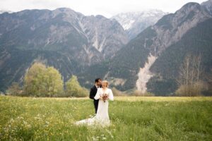 Wedding couple standing in a meadow before high mountains while the groom embraces the bride from behind