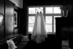 Black-and-white photo of a wedding dress hanging in front of a window