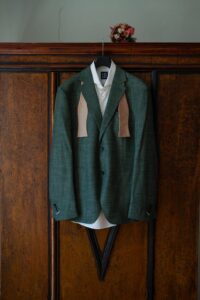 The groom’s dark green suit hanging in front of a rustic wooden wardrobe