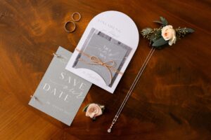 Angled flat lay of the invitation, jewelry, wedding rings, and floral details