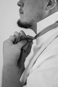 Black-and-white close-up of the groom tying his tie