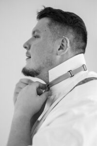 Black-and-white side view of the groom tying his tie