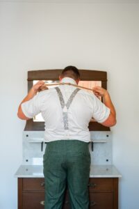 The groom stands before a mirror putting on his tie