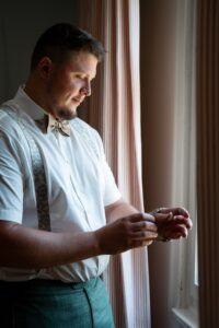 The groom looks at his watch while standing by the window