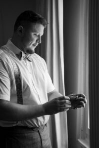Black-and-white photo of the groom looking at his watch by the window