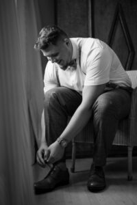 Black-and-white photo of the groom tying his shoes