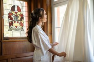 Side view of the bride looking at and touching her wedding dress by the window