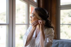 The bride puts on her earrings while looking out the window