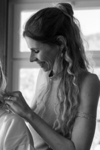 Black-and-white photo of the maid of honor fastening the bride’s necklace