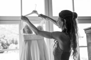 Black-and-white photo of the maid of honor taking the wedding dress off its hanger