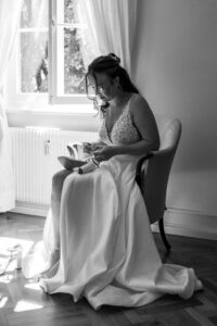 Black-and-white photo of the bride sitting on a chair while unfastening her shoes