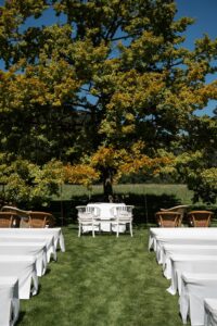 Wedding ceremony location beneath a large tree with white benches
