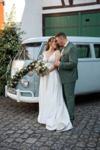 Bride and groom standing in front of a VW T2 bus as he hugs her from behind