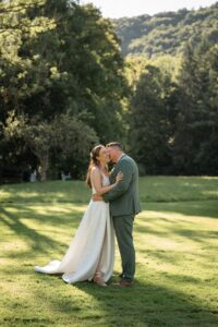 Full-body photo of the groom kissing his bride on the cheek