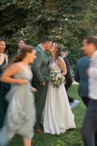 The wedding couple kisses in a meadow while bridesmaids and groomsmen move around them in motion blur