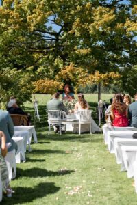 View from the aisle with guests on both sides and the wedding couple seated beneath the tree