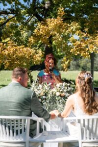 The wedding couple sits beneath a tree during the ceremony, listening to the officiant