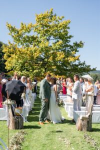 The wedding couple kisses at the end of the recessional in front of their guests and the large tree