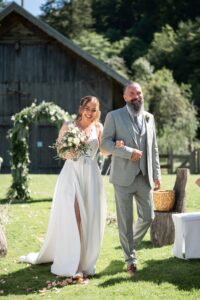 The bride walks past the floral arch with her father on the way to the ceremony