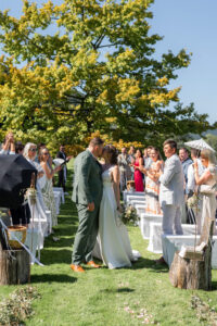 The wedding couple kisses at the end of the recessional in front of their guests and the large tree