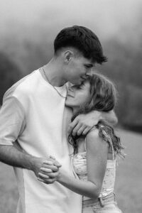 Young man wrapping his arm around his girlfriend’s neck while she cuddles against him