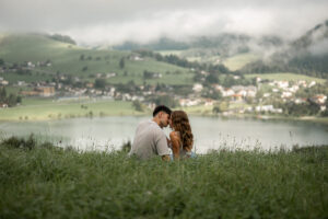 Couple sitting on a meadow overlooking a lake and a Tyrolean village