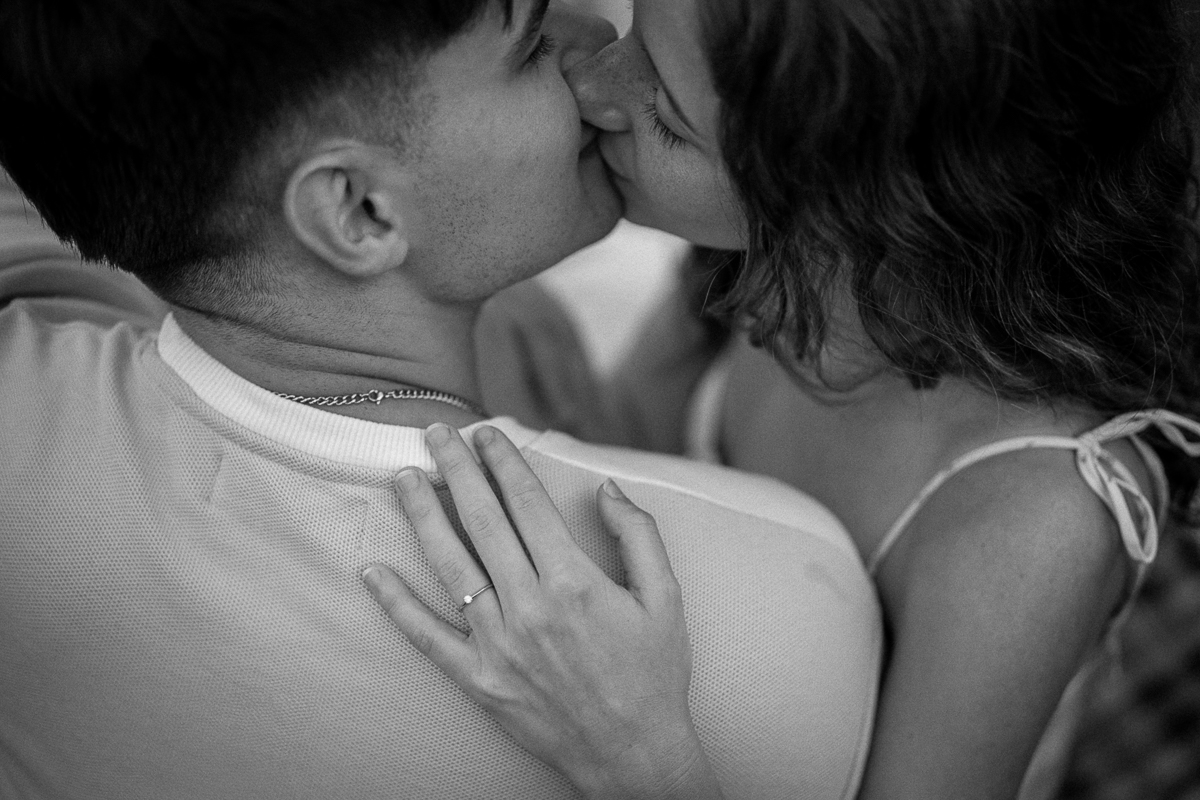 Over-the-shoulder photo of a couple kissing with a visible engagement ring