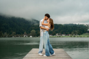 Young couple standing on a dock by the lake while embracing and smiling