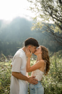 Young couple kissing in backlight beneath a tree with mountains and reeds in the background