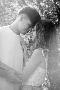 Close black-and-white photo of a couple embracing beside a tree with sunlight entering from the side