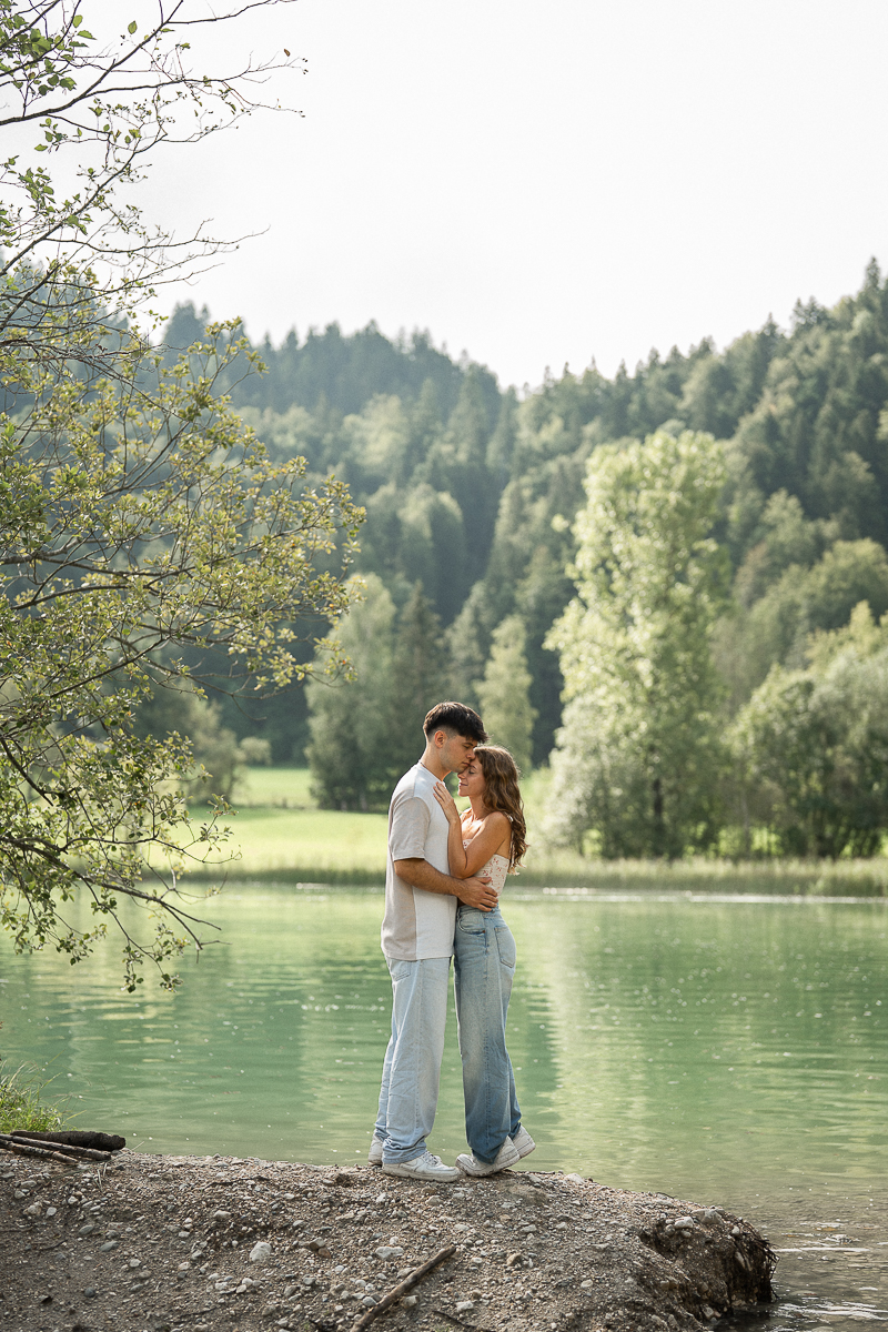 Couple embracing from a distance in front of a peaceful lake and lush nature