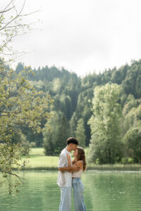 Young woman being kissed on the forehead by her fiancé in front of a reflective lake