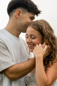 Young man holding his girlfriend’s cheek while smiling and whispering into her ear