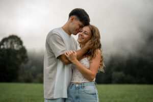 Young man embracing his fiancée from the side while holding her face and leaning his head against hers