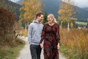 Young couple walking hand in hand between autumn trees while smiling at each other