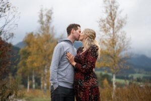Couple kissing in front of autumn trees while the woman rests her hand on his chest
