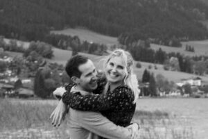 Black-and-white photo of a couple embracing in motion by a lake with slight motion blur and joyful laughter