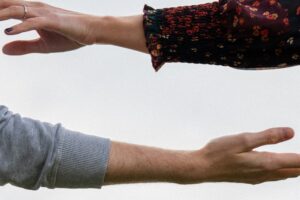 Side view of outstretched arms against the sky with hands facing each other